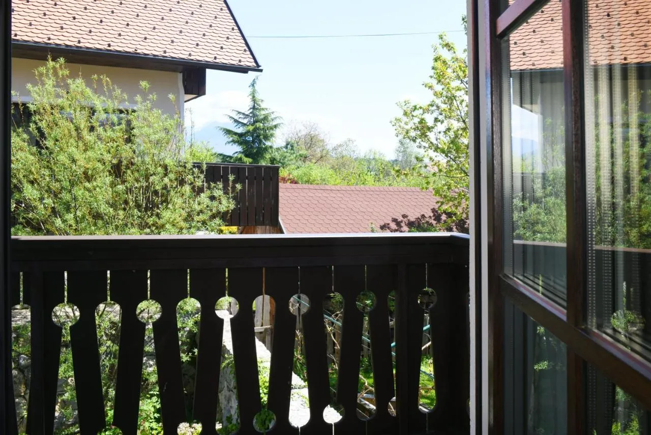 Pogled z balkona z rezljano ograjo na zelenje in strehe