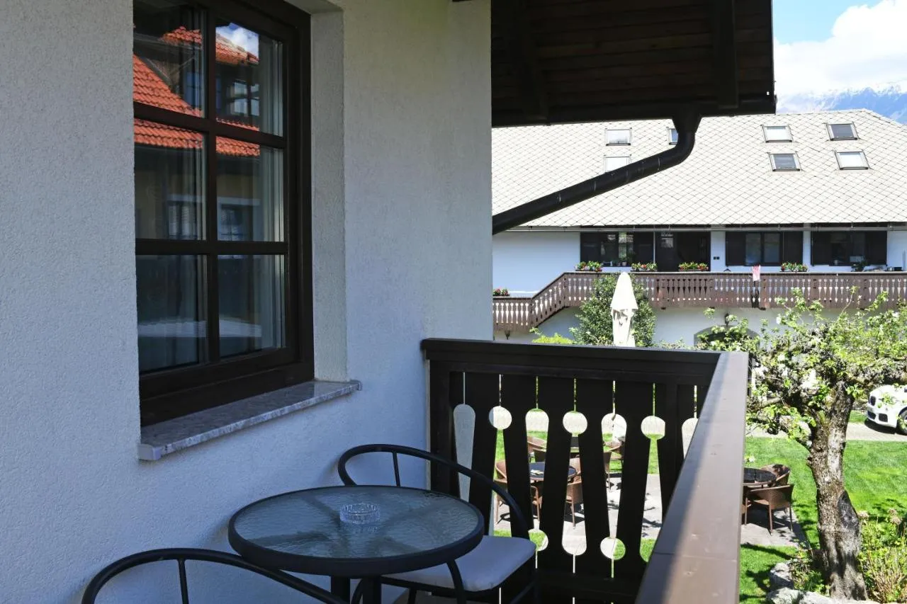 Balkon z mizico in stoli, pogled čez dvorišče na kmečko hišo in gore